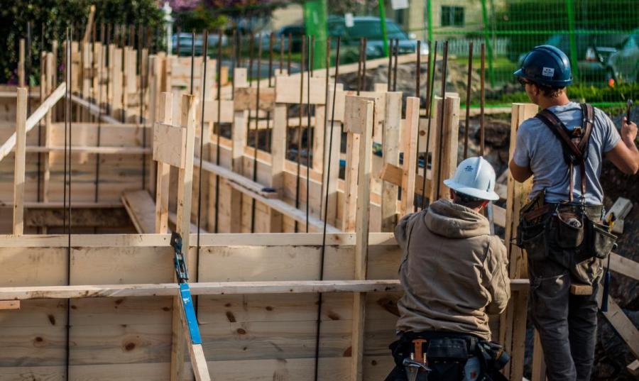 Construction workers building concrete framing for house foundation