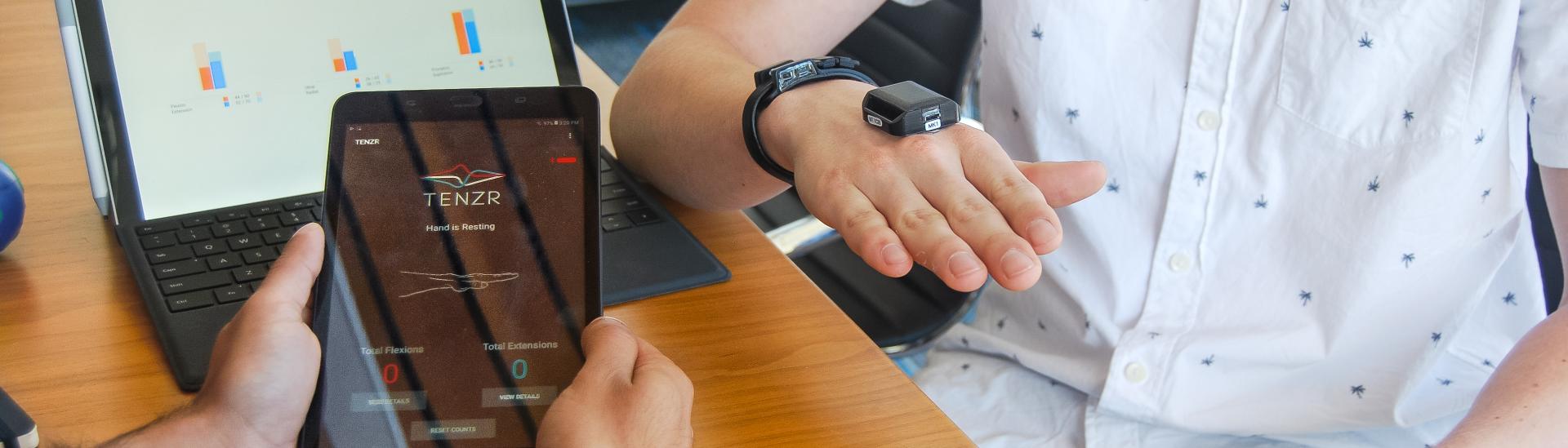 Person holding a tablet with health-related app open while other person has sensor on their hand